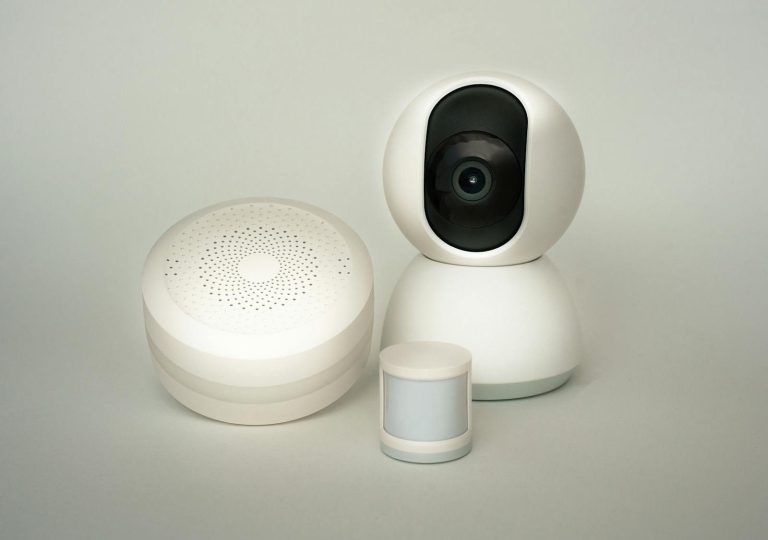 Modern smart home devices including a camera and sensors on a neutral background.